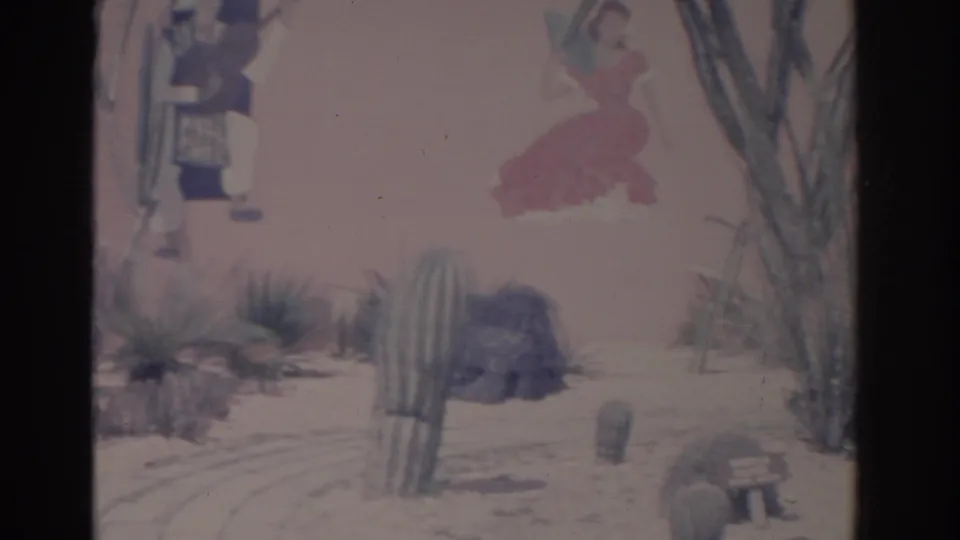 1962 Florida 8mm view of a cactus garden beside a pink wall with painted figures, including a woman in a red dress.