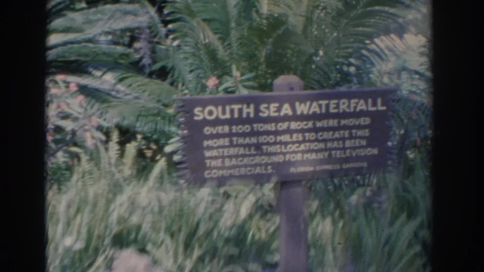 A handheld 8mm frame shows the South Sea Waterfall sign at Florida Cypress Gardens with lush plantings around it.