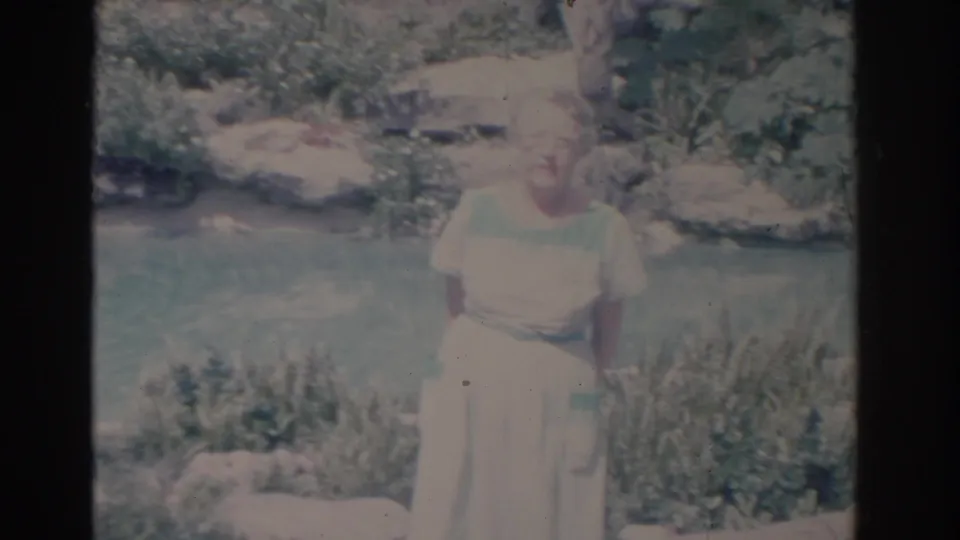 Faded 1962 Florida 8mm frame showing an adult woman posed near a landscaped water feature with rocks and plants.