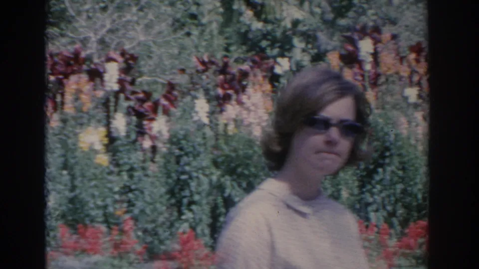 1962 Florida 8mm still showing a woman in sunglasses and a light top before red flowers and dense garden foliage.