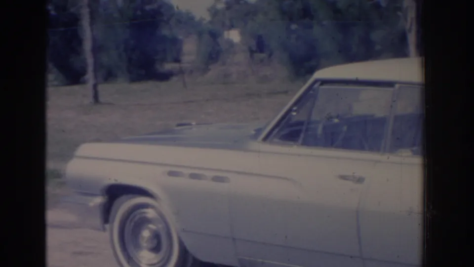 1962 Florida 8mm frame showing a light-colored American sedan parked on a grassy roadside near trees.