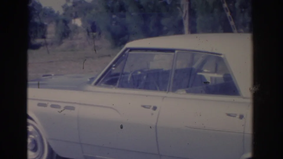 1962 Florida home-movie frame with a side view of a light-colored sedan near the exposition grounds.