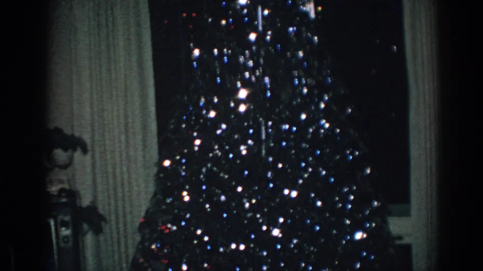 1962 8mm home-movie frame from Gary, Indiana showing a decorated Christmas tree glowing beside curtains and a window.