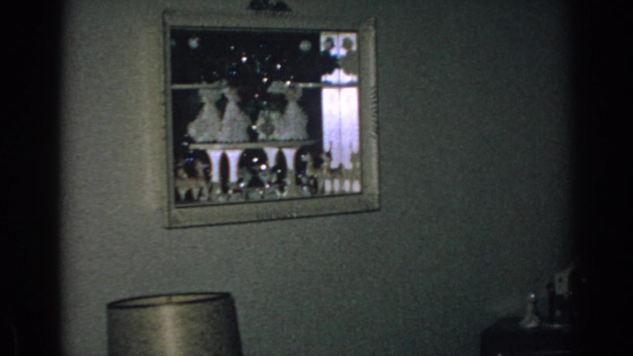 Framed holiday display on a wall above a lamp in a dim interior.