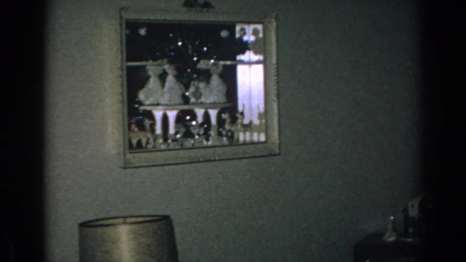 Gary, Indiana home interior with a framed seasonal display on the wall and a lamp below, captured on 8mm film in 1962.