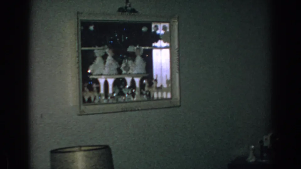 Close 1962 home-movie view of a framed Christmas display on an interior wall, with a lamp shade visible below.