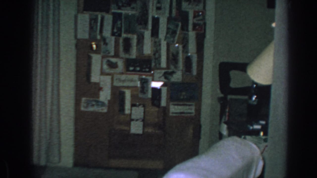 Dim room with a crowded wall of photographs, curtain, couch edge, and lamp at right.