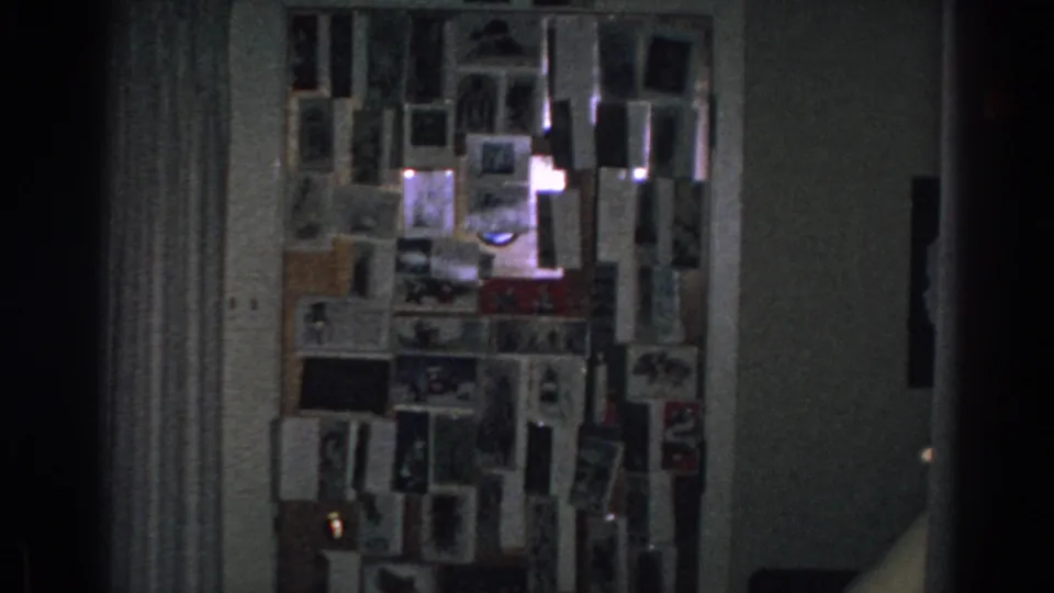 The final sampled frame keeps the Gary, Indiana room corner in view, with a photo-covered wall, curtain, and lamp in soft 8mm grain.