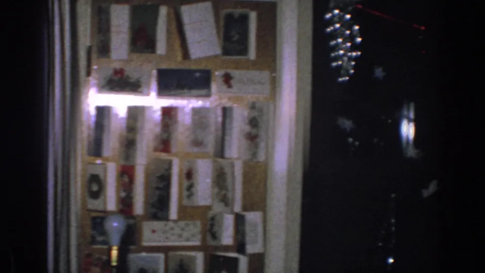1962 Gary, Indiana interior frame with a card-covered board, curtains, and glimmering holiday lights in the dark area at right.