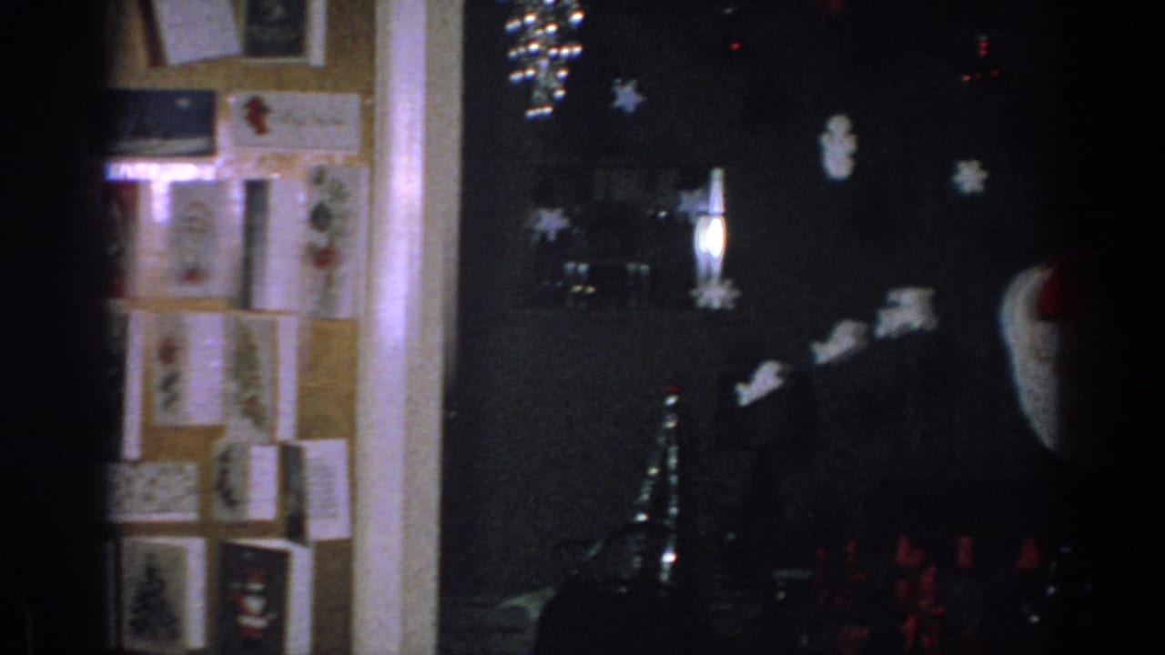 1962 Gary, Indiana home-movie frame showing a corkboard of Christmas cards and the edge of a decorated interior.