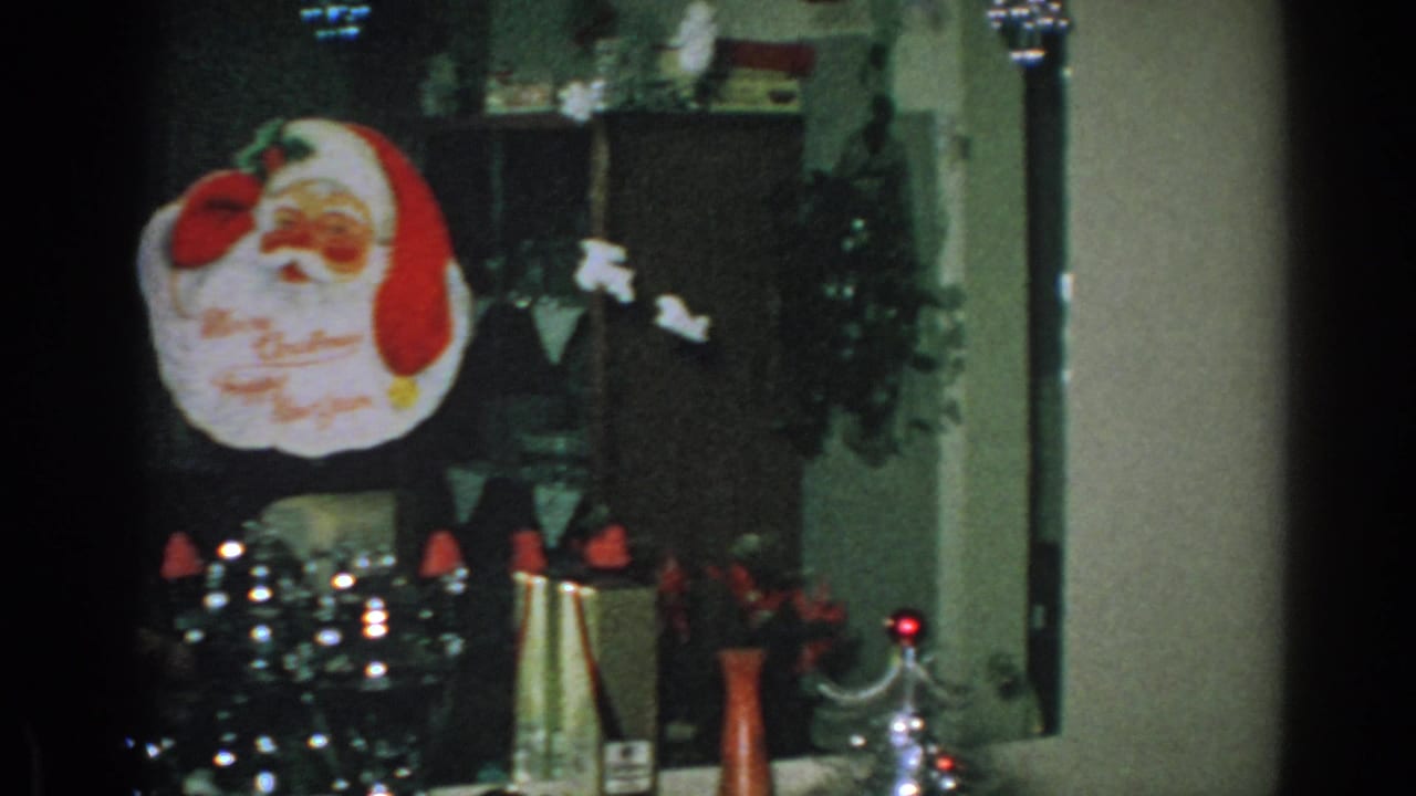 1962 Gary, Indiana home interior with a Santa wall hanging, holiday greenery, and tabletop decorations in dim 8mm footage.