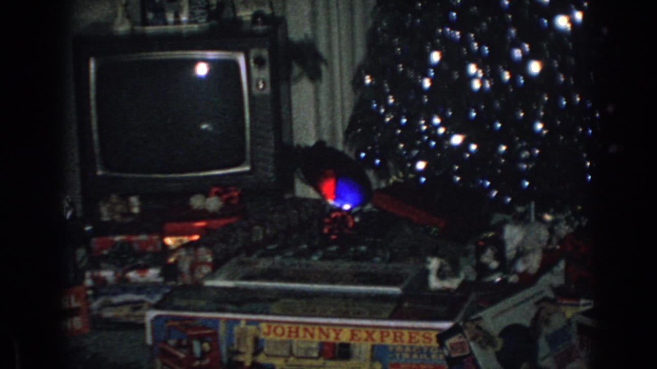 Christmas tree with presents, a television set, curtains, and toy boxes in a dim living room.