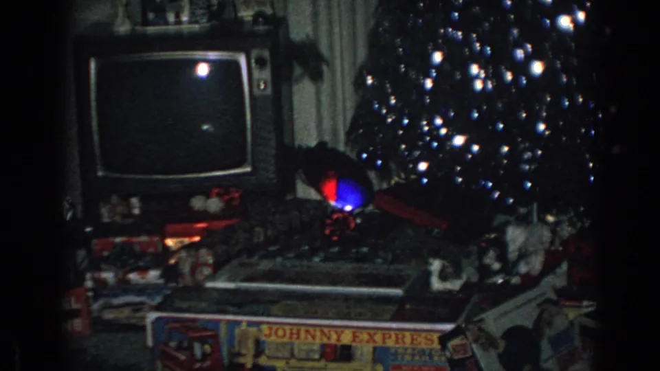 1962 Gary, Indiana home-movie frame showing a dim living room with a black-and-white television beside a decorated Christmas tree and boxed gifts on the floor.