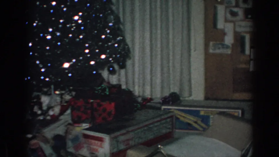 1962 Gary, Indiana home-movie frame showing Christmas presents and toy boxes near a decorated tree, with curtains and an open doorway visible at the side.