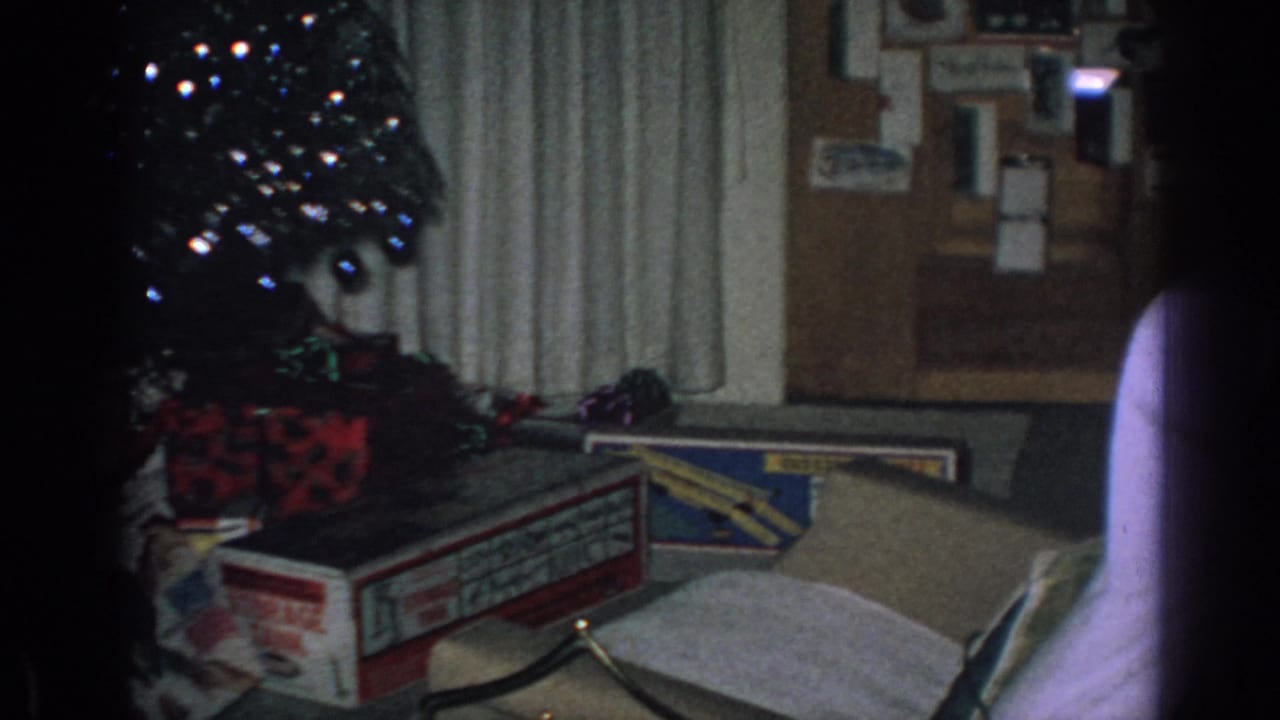 Living room corner with Christmas tree, wrapped gifts, open boxes, curtains, and bulletin board.