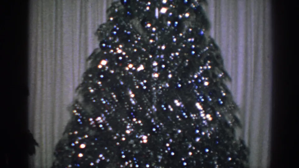 1962 Gary, Indiana home-movie frame with sparkly tree branches, ornaments, and bright light reflections against pale curtains.