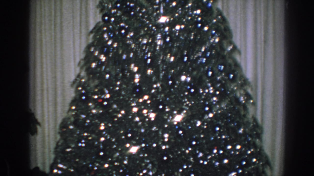 Lit Christmas tree with tinsel and curtains behind it.