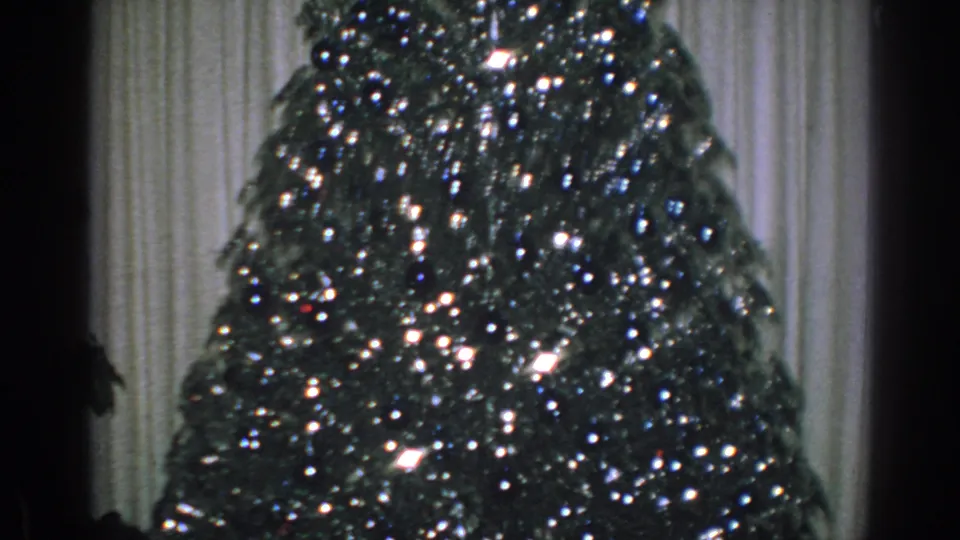 1962 Gary, Indiana 8mm frame showing a lit Christmas tree with reflective tinsel against pale curtains.