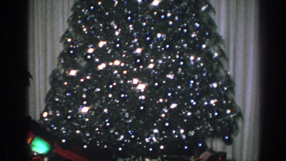 1962 Gary, Indiana 8mm frame with a lit Christmas tree partly divided by a dark vertical camera-edge shadow.