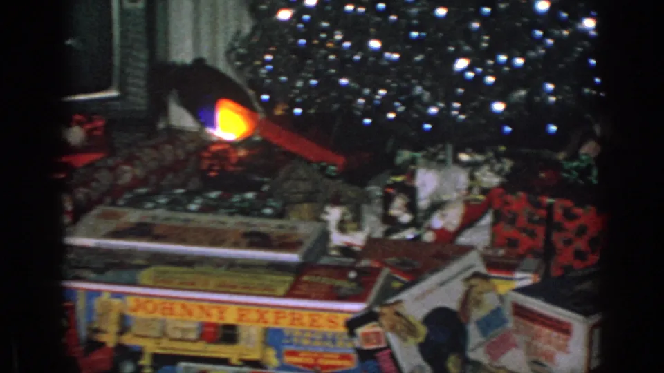 1960s 8mm frame of boxed toys and wrapped presents beneath a decorated Christmas tree in a private home.