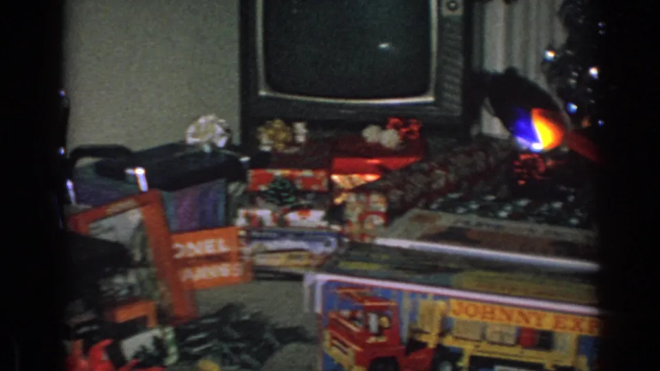 Gary, Indiana Christmas morning frame with a television, wrapped presents, and branded toy boxes in a private 1962 home interior.