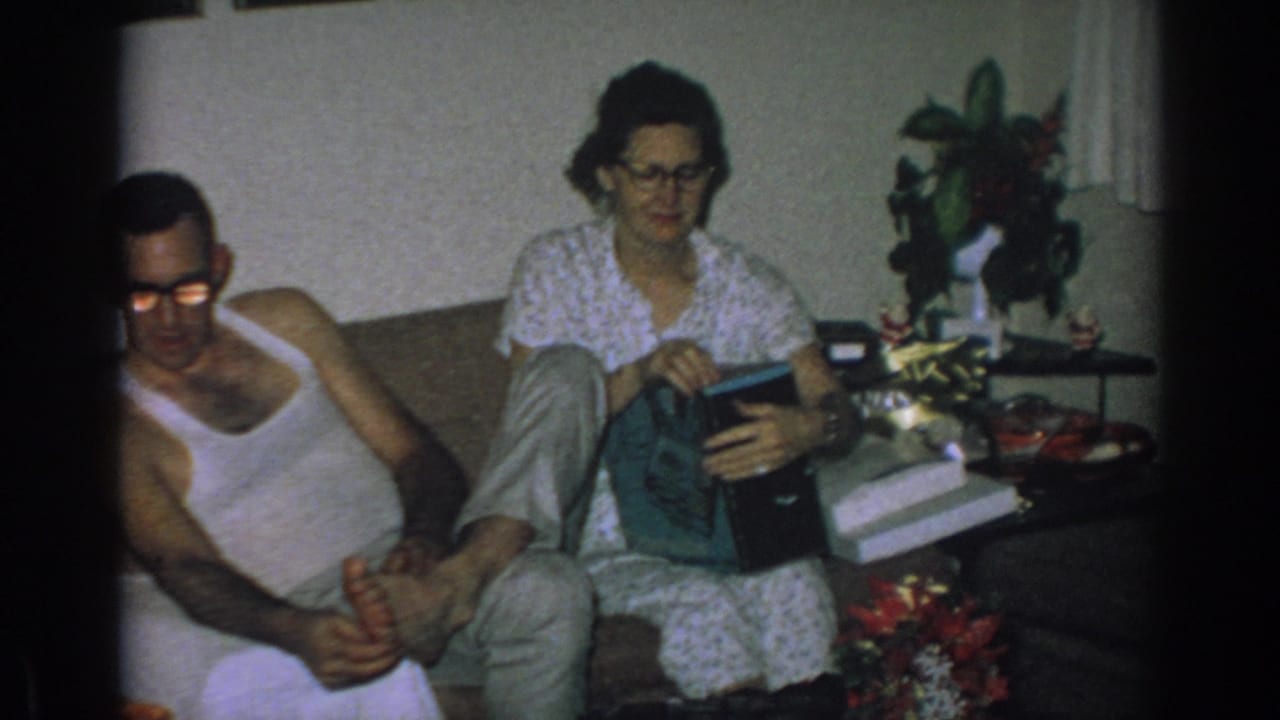 Woman seated on couch opening a gift while a man sits beside her in a living room.