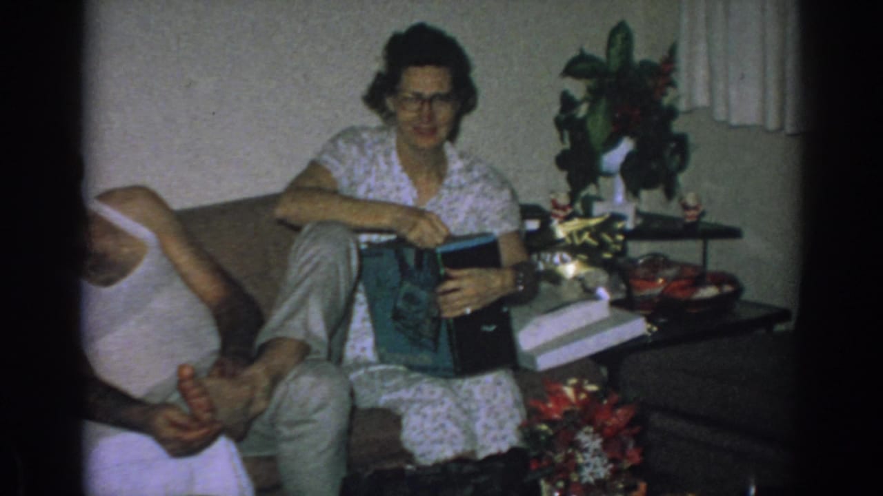 The woman sits with a gift or album open on her lap in the Gary, Indiana home interior, with holiday items on the side table.