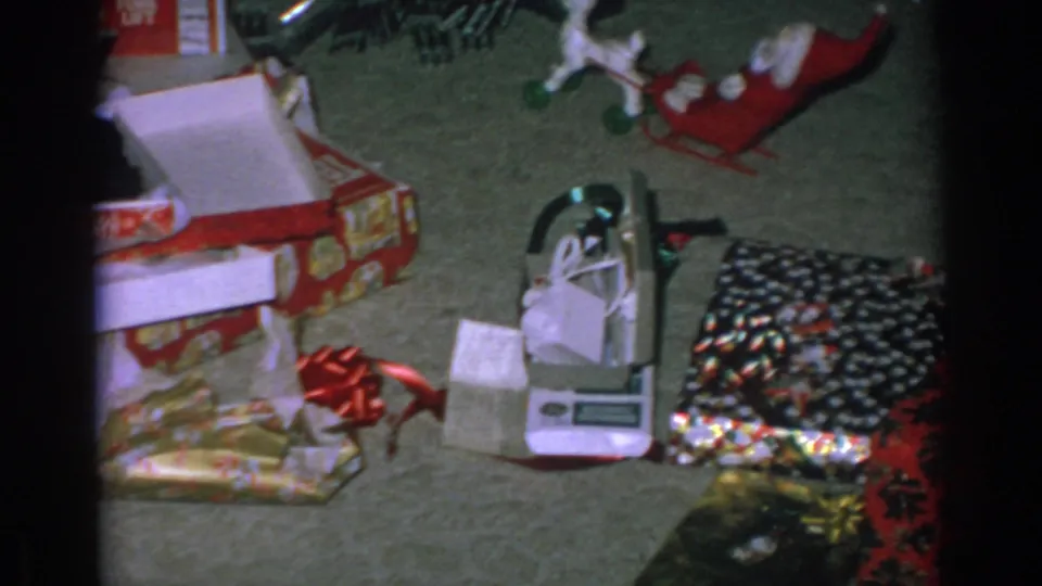 Gary, Indiana holiday home-movie frame with opened gift boxes, shiny wrapping, a small device or toy, and the Santa sleigh decoration.