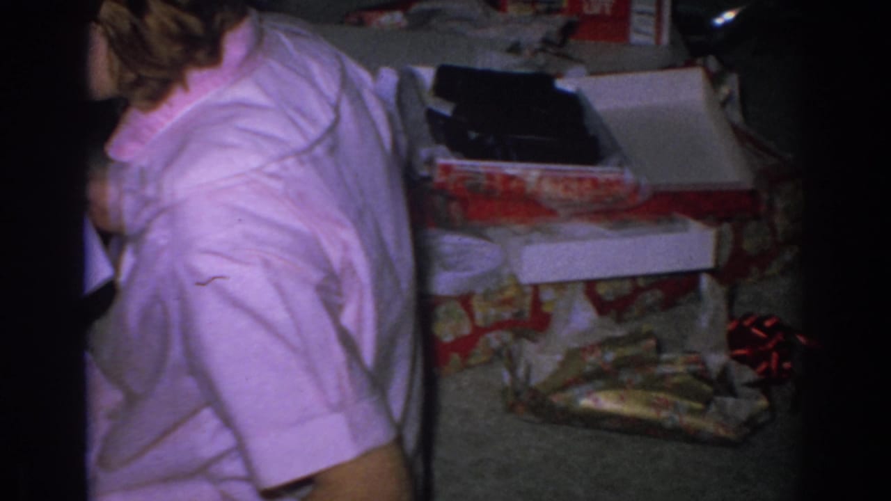 Woman in a pink shirt sits near opened Christmas gifts and wrapping paper on a carpeted floor.