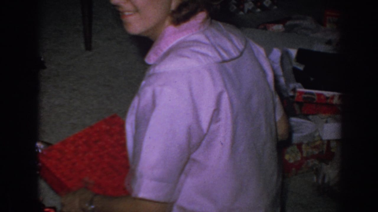 Woman in a pink shirt holds a red wrapped package near Christmas boxes on the floor.
