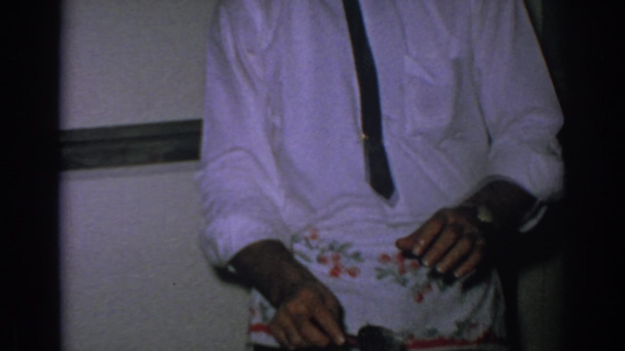 Man in white shirt, tie, and apron holds a utensil near a serving dish.