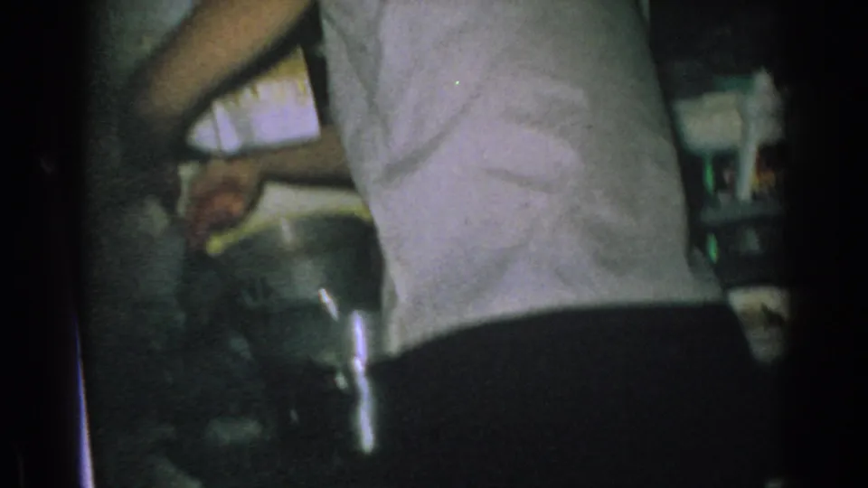 A person in a light sleeveless top leans near the kitchen work area in the 1962 Gary, Indiana home movie.