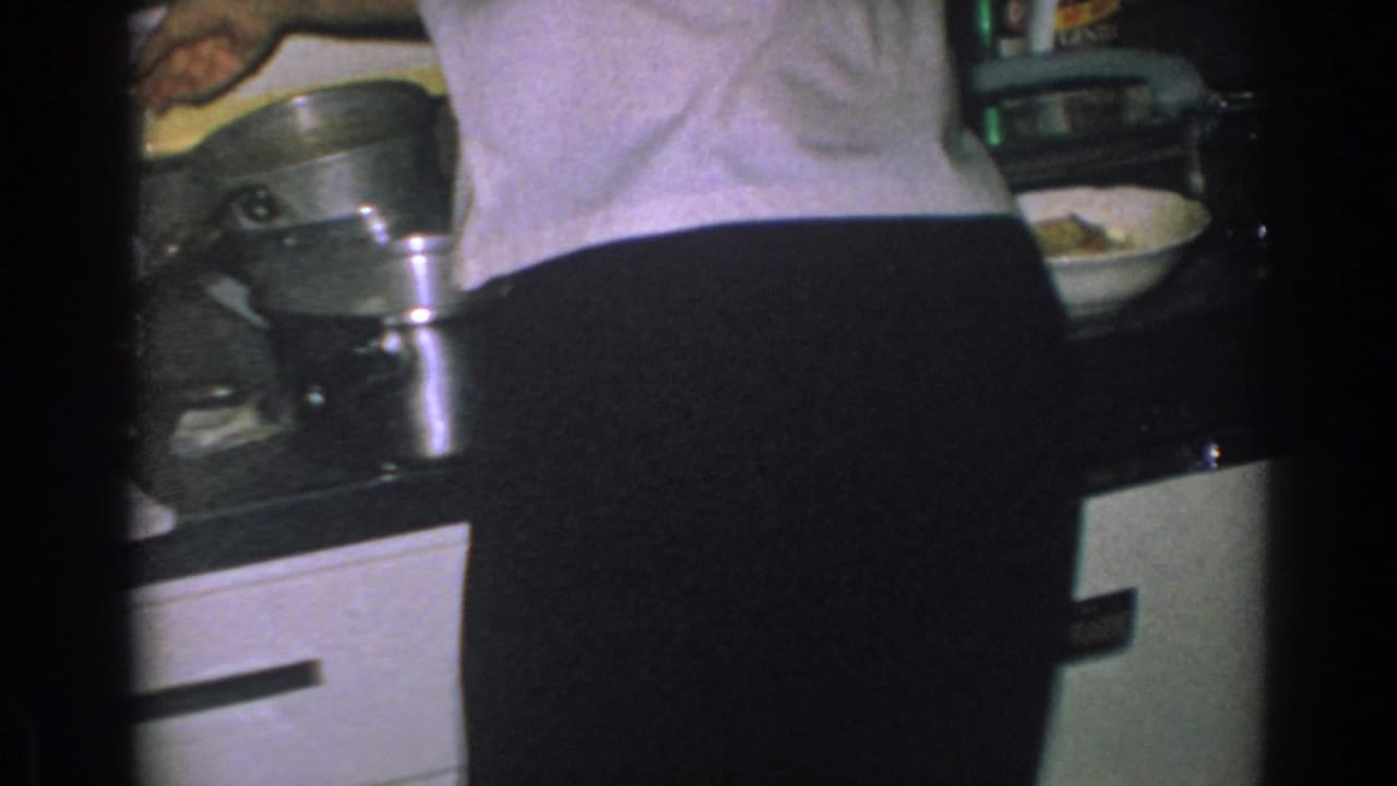 Woman seen from behind working at a kitchen counter with pots and cabinets nearby.