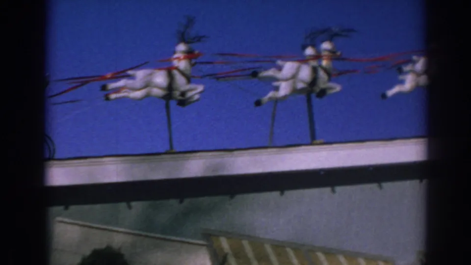 1962 Gary, Indiana 8mm frame centered on white reindeer figures and red reins along the rooftop holiday display.
