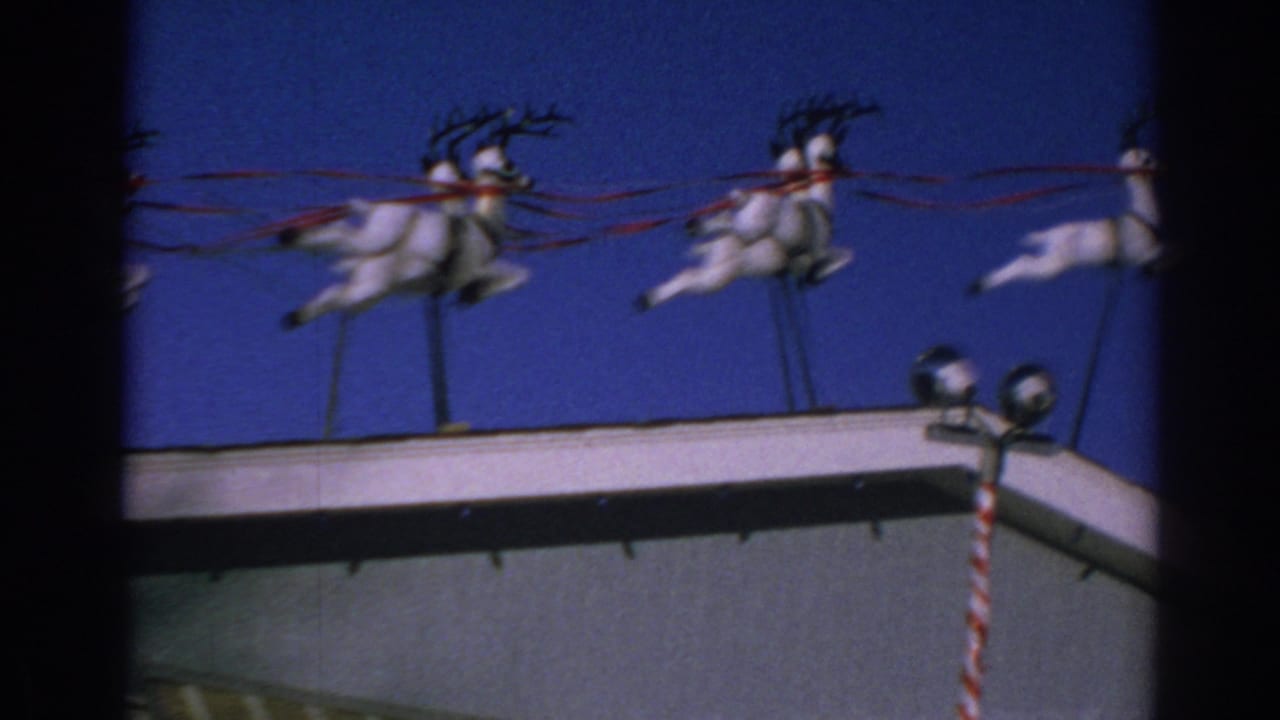 White reindeer roof decoration with red ribbon reins against a blue sky.