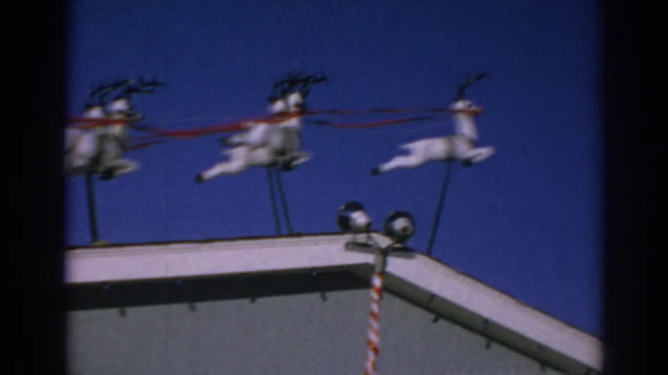 1962 Gary, Indiana frame with roof-mounted reindeer figures, red ribbon reins, and a candy-cane striped pole near a light fixture.