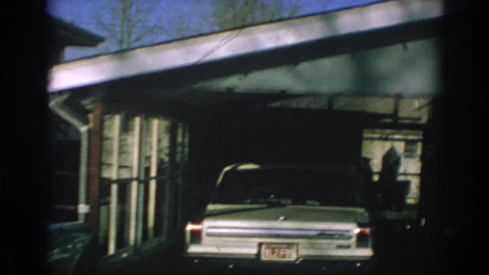 1962 Gary, Indiana frame showing the house exterior, garage, parked period car, roof edge, and a partial holiday decoration above.