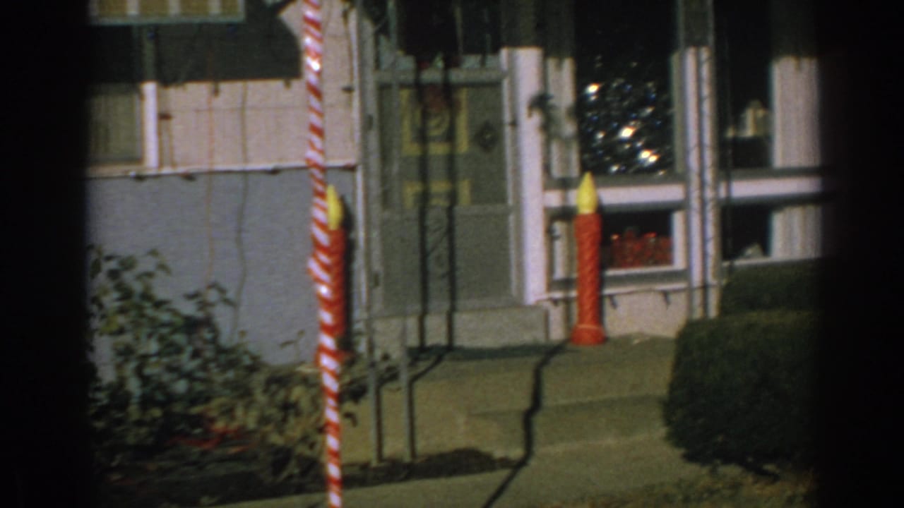 Front porch with candy cane and candle Christmas decorations beside windows and shrubs.