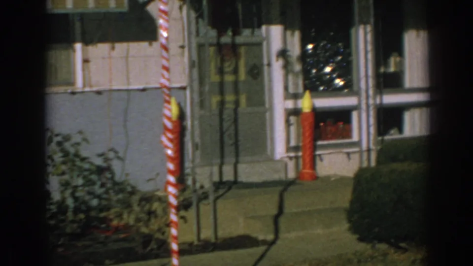 1962 Gary, Indiana home-movie frame showing a decorated front porch with a striped candy cane, red candle, windows, lawn, and shrubs.