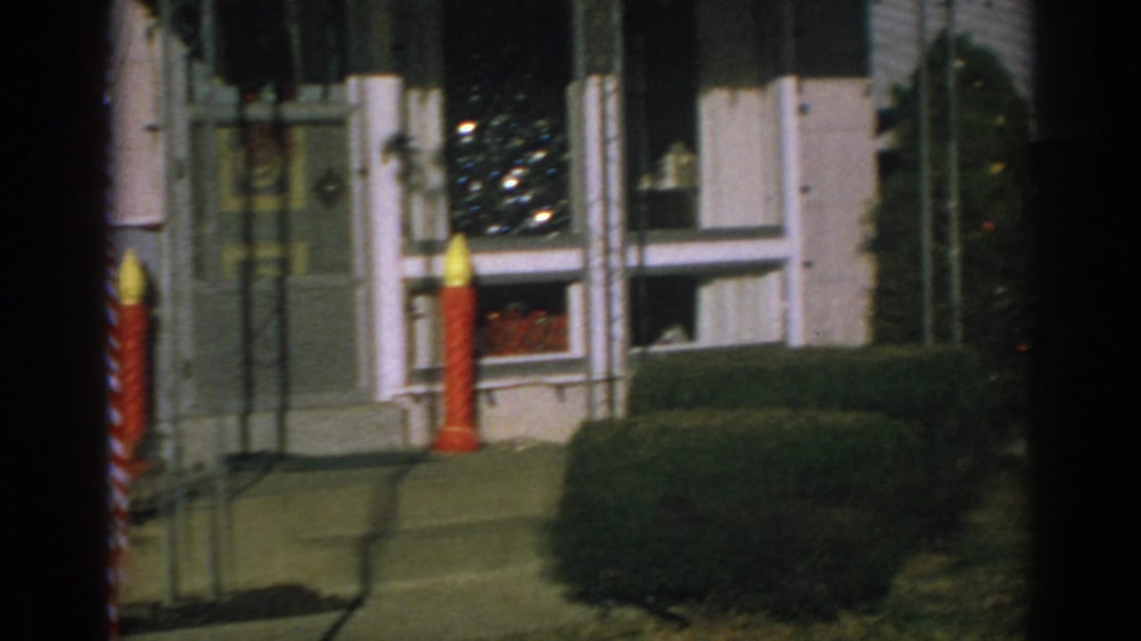 Front door and windows with a red candle decoration, hedge, lawn, and Christmas tree indoors.