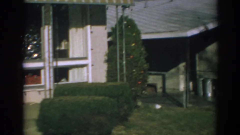 1962 Gary, Indiana frame from the pan showing the side of the decorated house, including a hedge, lawn, window, and roof overhang.
