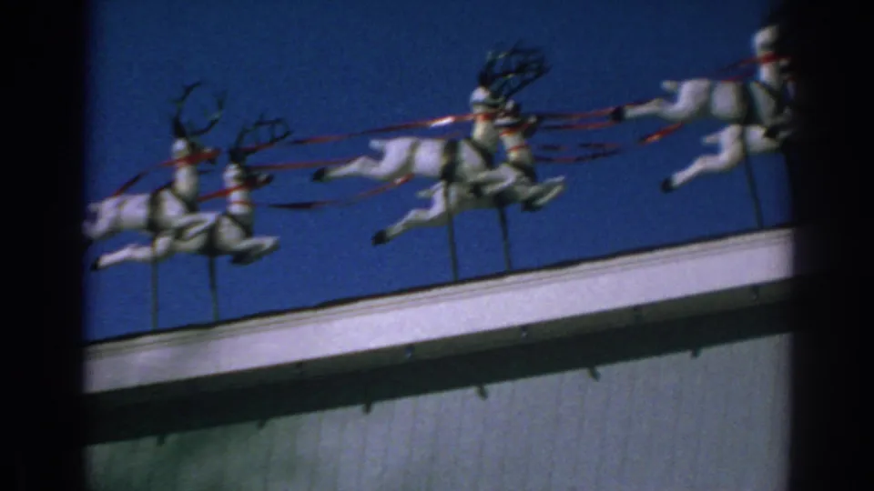 1962 Gary, Indiana home-movie frame with white reindeer figures and red reins crossing a rooftop holiday display.