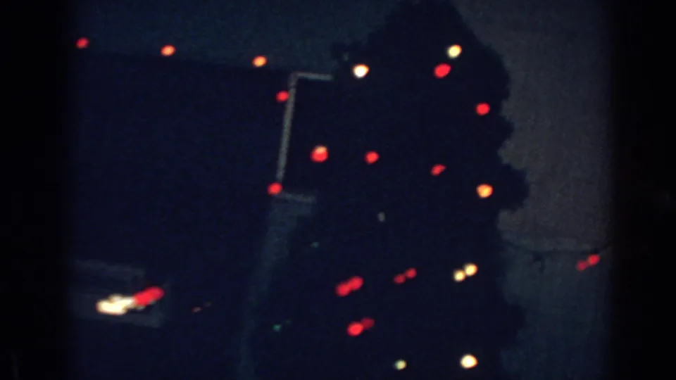 Nighttime 8mm frame from Gary, Indiana showing a decorated exterior with glowing Christmas lights in soft focus.