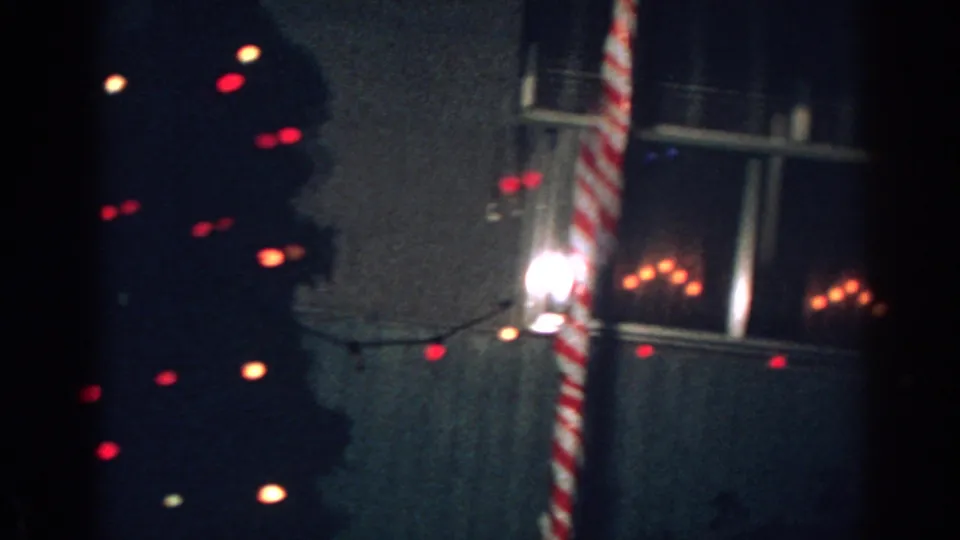 1962 home-movie frame with a striped candy cane decoration, window light, and outdoor Christmas bulbs in Gary, Indiana.