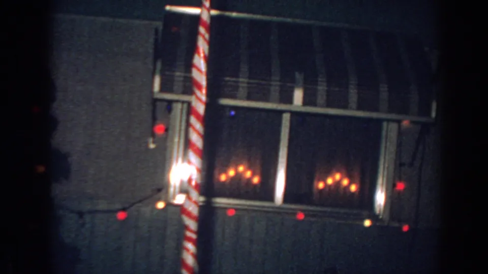 Gary, Indiana 1962 frame showing a window with warm light, a candy cane decoration, and red Christmas bulbs outside.