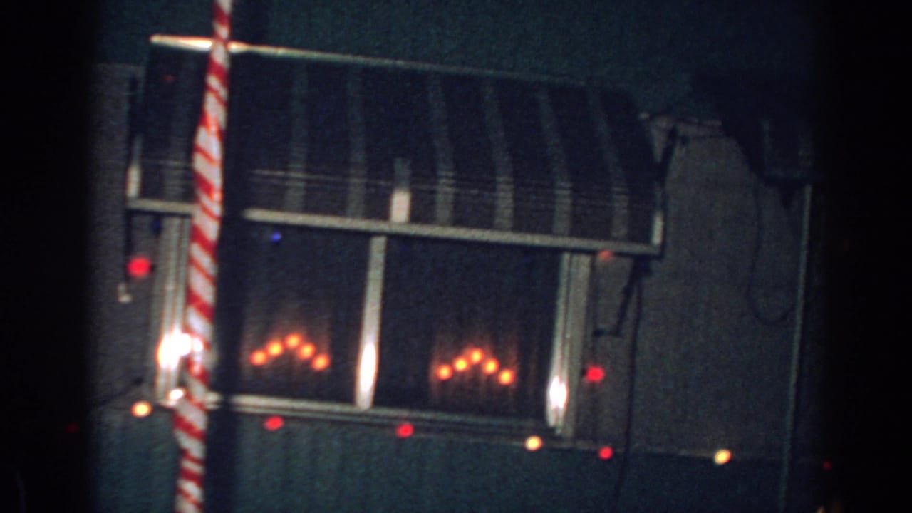1962 Gary, Indiana 8mm frame showing a dim nighttime house exterior with a striped awning, red holiday lights, and a red-and-white candy-cane-style pole.