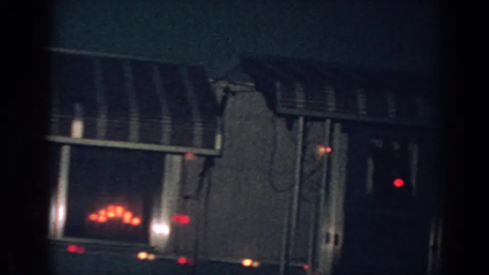 1962 Gary, Indiana home-movie frame with dark windows, a striped awning, and small red Christmas lights glowing against the house exterior.