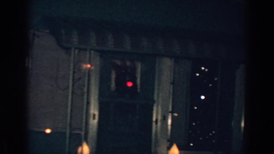 1962 Gary, Indiana 8mm frame showing a shadowed residential exterior with window reflections, red points of light, and partial striped awning details.