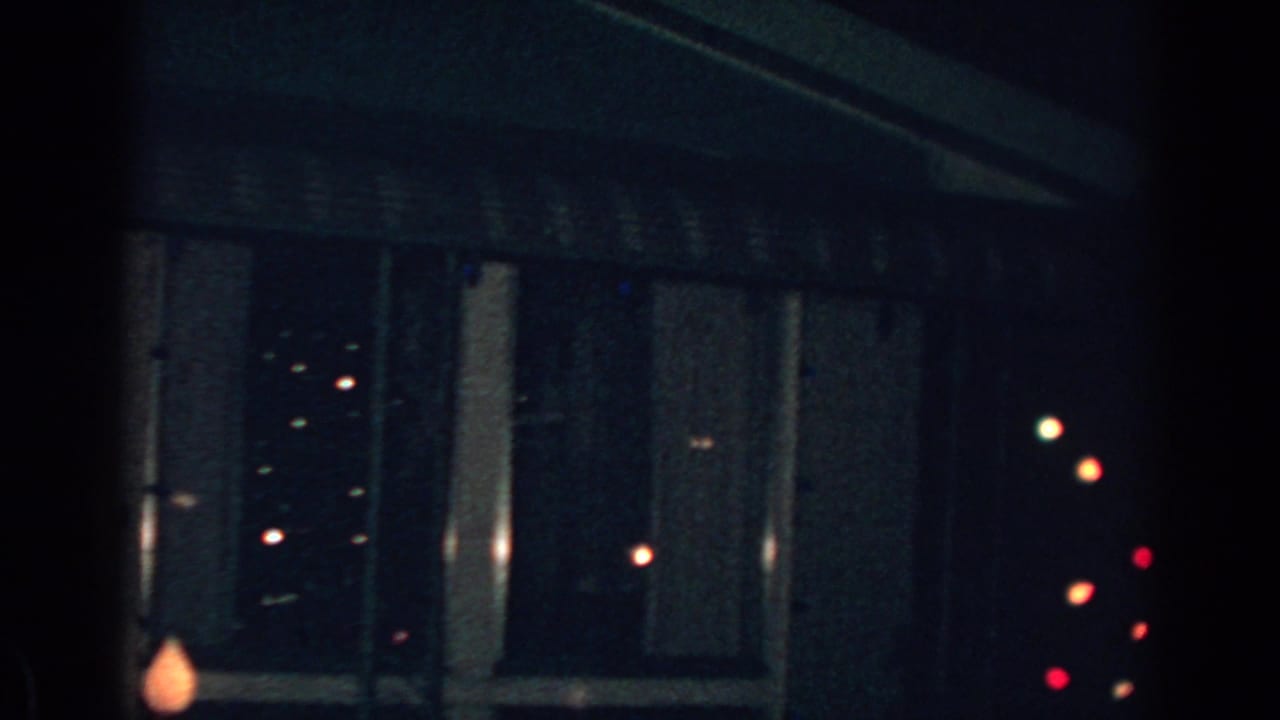 Dark house window with striped awning and small Christmas bulbs at night.