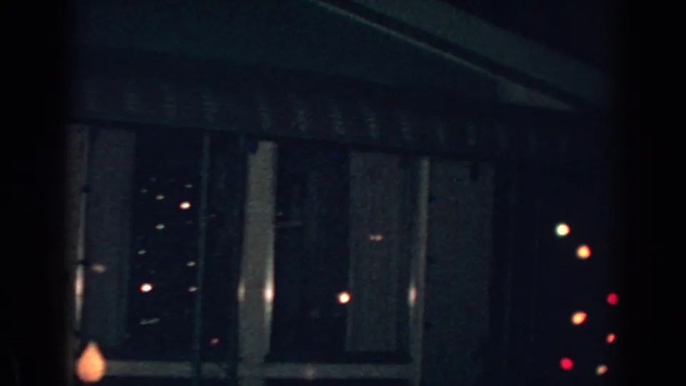 1962 Gary, Indiana home-movie frame showing a dark house window, striped awning, and scattered holiday bulbs at night.